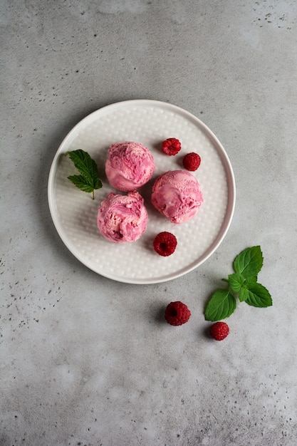 Homemade raspberry ice cream with fresh berries on gray ceramic plate. Top view.