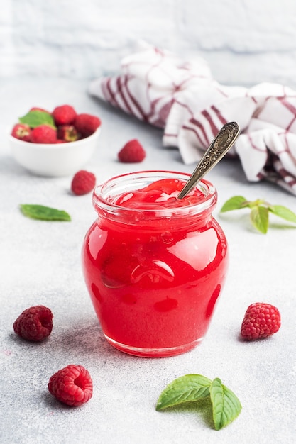 Homemade raspberry jam in a glass jar and fresh raspberries with mint