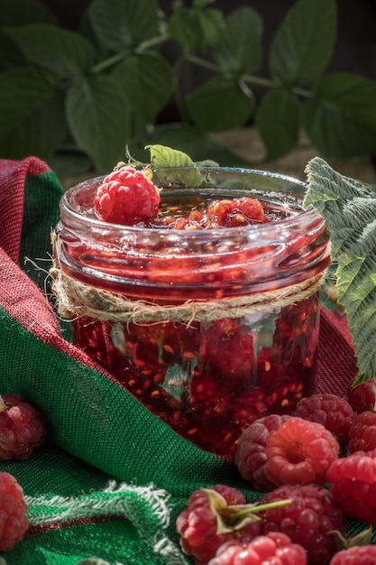 Homemade raspberry jam in a jam jar raw raspberries on a green napkin