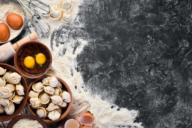 집에서 만든 라비올리 만두 밀가루 계란 반죽을 검정색 배경 위에 놓습니다. 무료 복사 공간