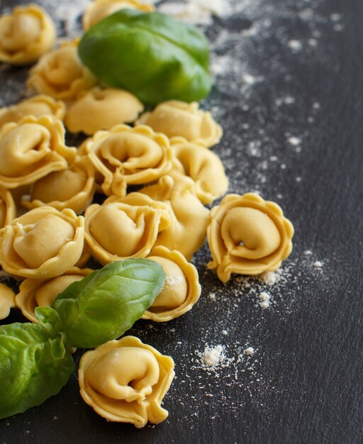 Homemade raw Italian tortellini and basil on a dark table close up