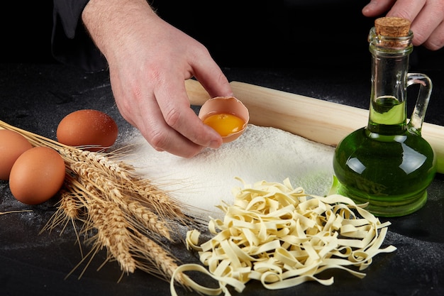 Homemade raw noodles made from flour, egg on wooden bowl on black