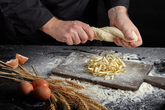 Homemade raw noodles made from flour, egg on wooden bowl on black