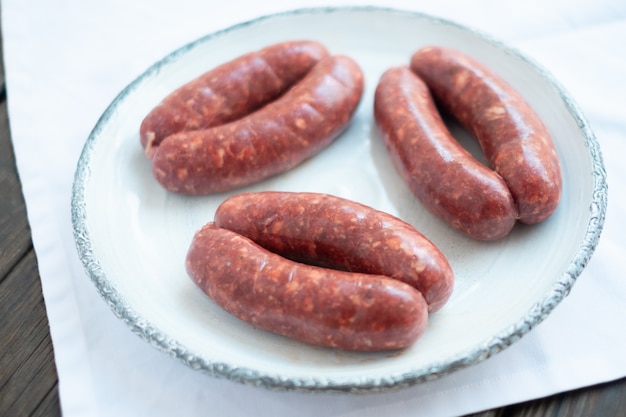 Homemade raw sausages on white plate for grill