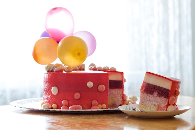 Homemade red birthday cake with air baloons. Slice of a red velvet cake on a plate.