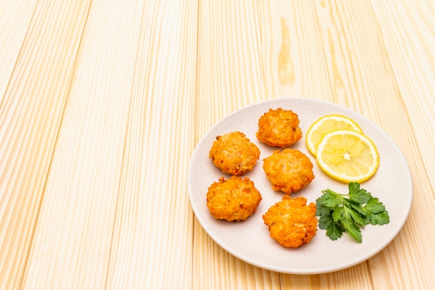 Foto crocchette di pesce rosse casalinghe con il limone e il prezzemolo in piatto ceramico. sulla superficie di legno, copia spazio.