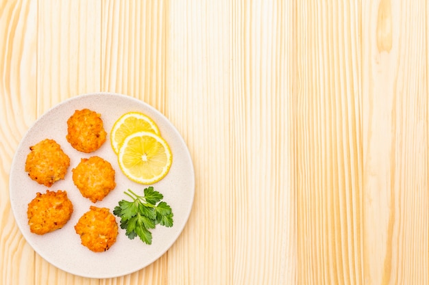 Crocchette di pesce rosse casalinghe con il limone e il prezzemolo in piatto ceramico. sulla superficie di legno, vista dall'alto, copia spazio.