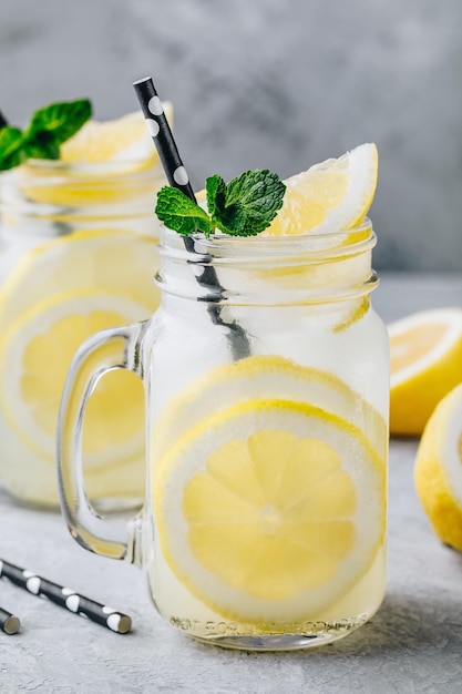 짚과 민트가 든 메이슨 항아리에 레몬 조각과 얼음을 넣은 신선한 여름 레모네이드 음료