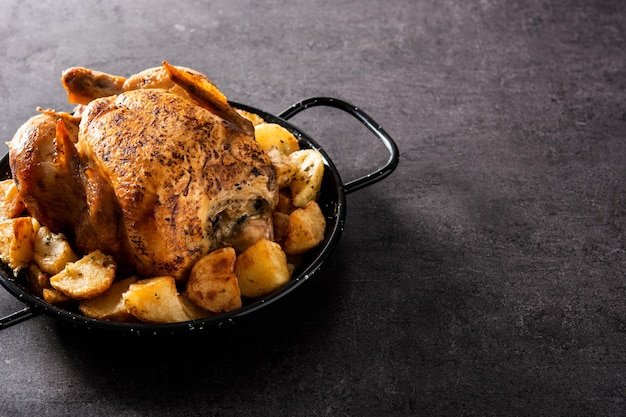 Homemade roasted chicken with potatoes on black background