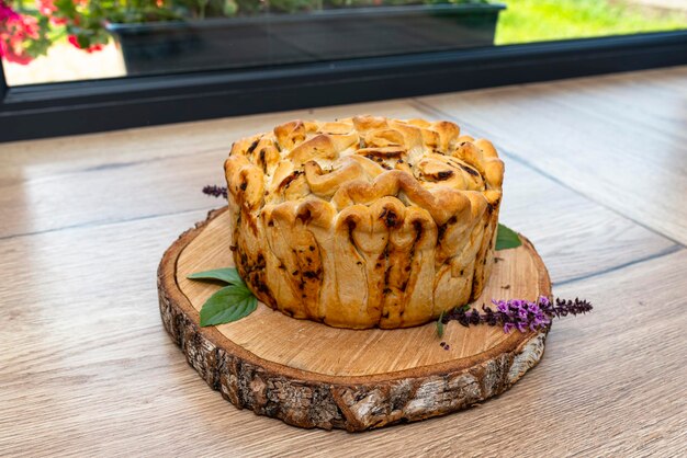 Домашний круглый хлеб с чесночным маслом и травами, лежащий на деревянной доске с листьями базилика