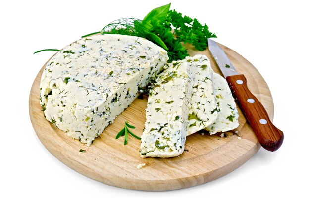 Homemade round cheese with herbs and spices cut into slices, knife on a round wooden board isolated on white background