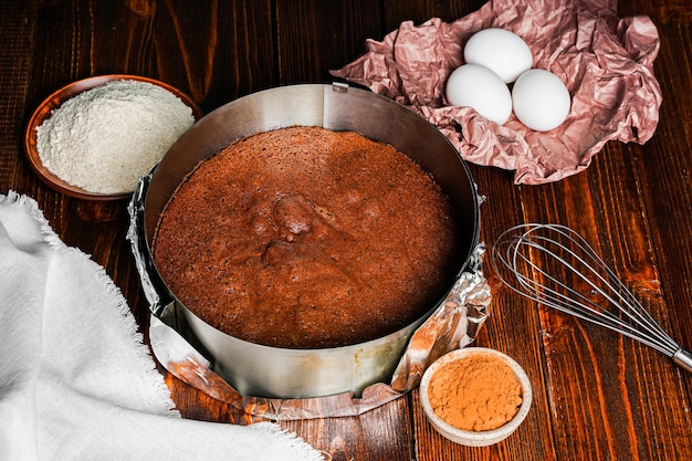 Homemade round chocolate sponge cake or chiffon cake on baking
paper so soft and delicious with ingredients eggs flour milk on
wood table homemade bakery concept for background and
wallpaper