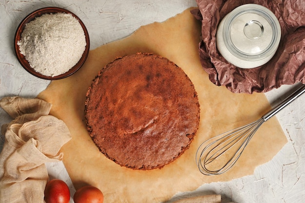 Homemade round chocolate sponge cake or chiffon cake on baking paper so soft and delicious with ingredients eggs flour milk on wood table Homemade bakery concept for background and wallpaper