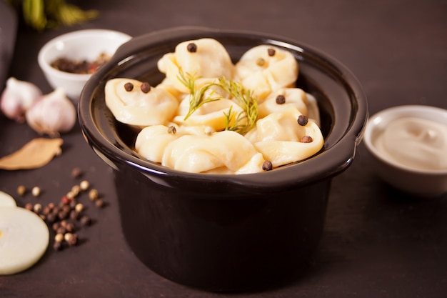 Homemade russian pelmeni meat dumplings italian ravioli in the small black pan.