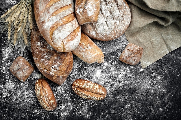 Homemade rye bread sprinkled with flour and various grains and seeds on a black background with spikelets of wheat or rye and oats