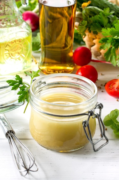 Foto condimento per insalata fatto in casa vinaigrette con senape e olio d'oliva su un tavolo di legno da cucina bianca