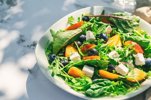 homemade salad with nectarines blueberries arugula and feta cheese on white marble background