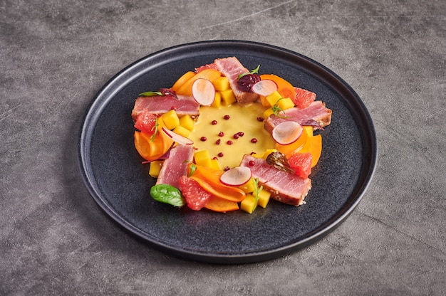 Homemade salad with tuna steak, mango sauce, herbs and spices on a dark plate, close up, food decorating concept