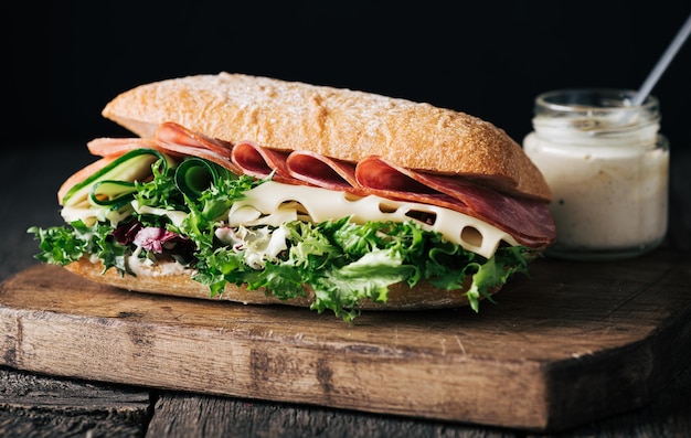 Homemade sandwich with ham cheese and lettuce leaves on dark wooden background selective focus