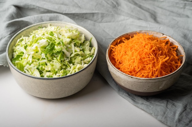 Домашняя квашеная капуста в стеклянной банке на сером столе. Нарежьте зеленую капусту и морковь для щей.