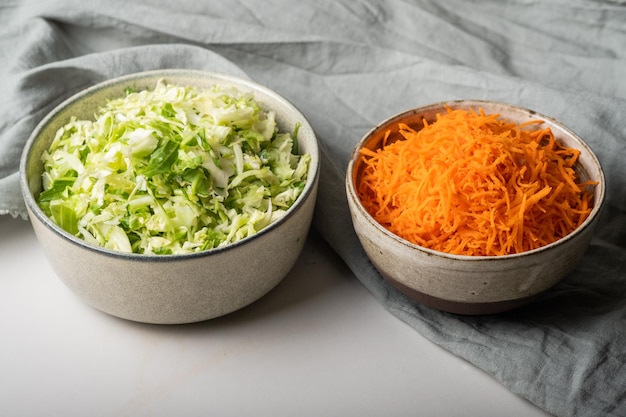 Homemade sauerkraut in a glass jar on a gray table.Cut green cabbage and carrots for cabbage soup.