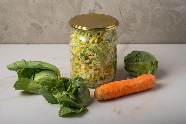 Homemade sauerkraut in a glass jar on a gray table.Cut green cabbage and carrots for cabbage soup.