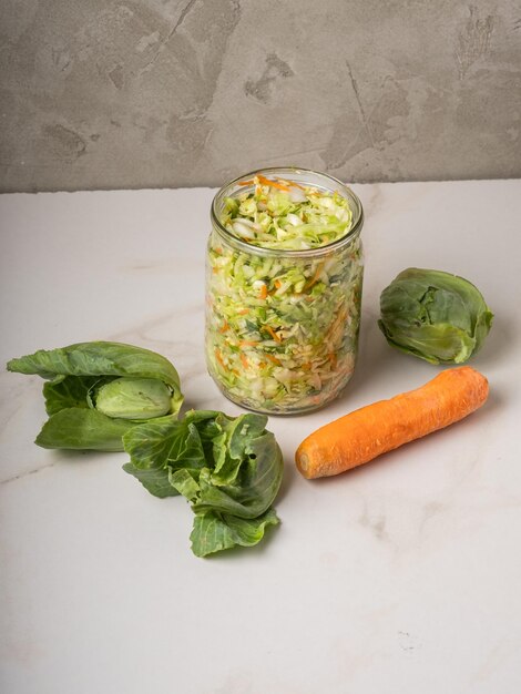 Homemade sauerkraut in a glass jar on a gray table.Cut green cabbage and carrots for cabbage soup.