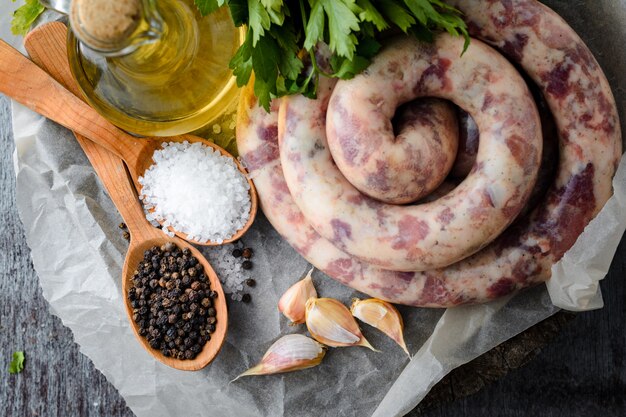 Homemade sausages, spices, garlic, olive oil and parsley on a wooden table.