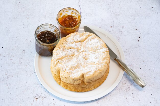 Homemade Savoie cake on a pretty white porcelain dish with jam in a jar