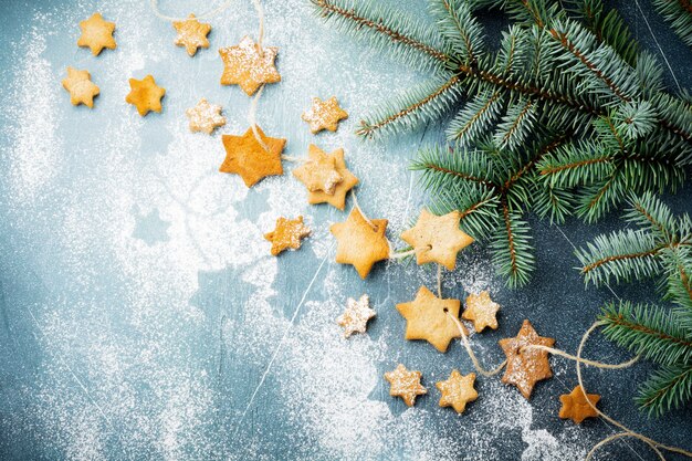 Homemade shortbread star shape sugar with sugar powder and branch of fit-tree on thread over blue texture surface.  Christmas or New Year. Top view with space.