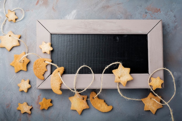 Homemade shortbread star shape sugar with sugar powder and branch of fit-tree on thread over blue texture surface.  Christmas or New Year. Top view with space.