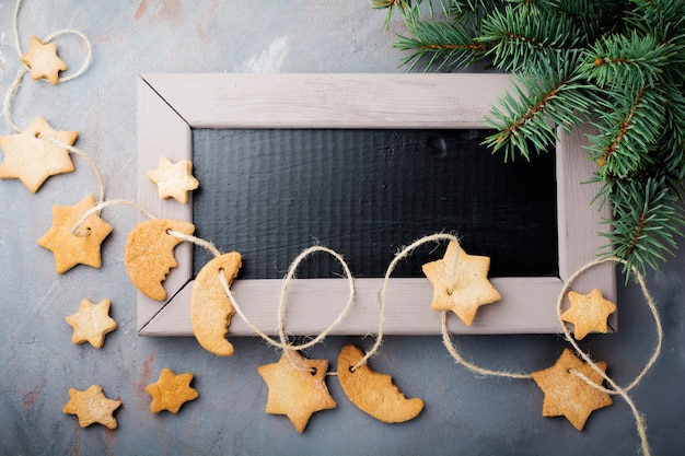 Homemade shortbread star shape sugar with sugar powder and branch of fit-tree on thread over blue texture surface.  Christmas or New Year. Top view with space.