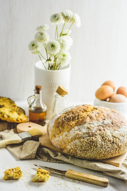 Pane a lievitazione naturale fatto in casa, alcune uova, olio, sesamo, tagliere di legno, coltello di legno e tovagliolo.