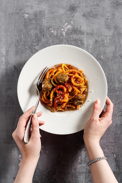 Foto spaghetti fatti in casa con salsa di pomodoro parmigiano e polpette su fondo scuro e mani femminili
