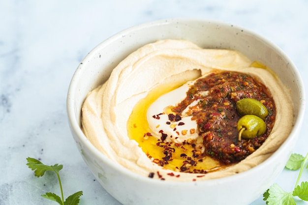 Homemade spicy hummus with tahini and olive oil in bowl white marble background Israeli traditional food