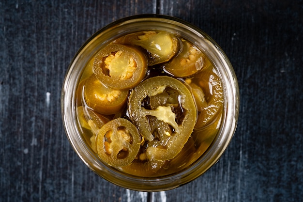 Homemade spicy jalapeno chillies marinated and sliced in a glass bowl on a dark wooden table