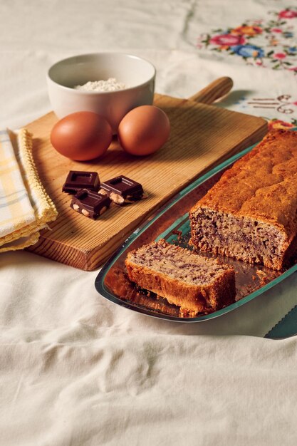 Homemade sponge cake on a white tablecloth with some ingredients eggs chocolate and flour