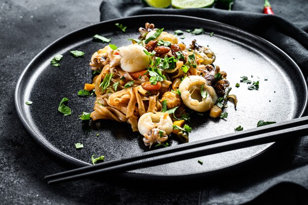 Homemade stir fry damage noodles with seafood and vegetables in a plate. Black background. Top view