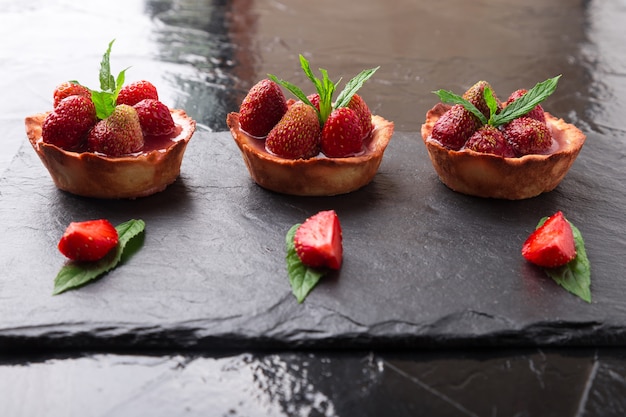 Homemade strawberries tarts on slate plate, black 