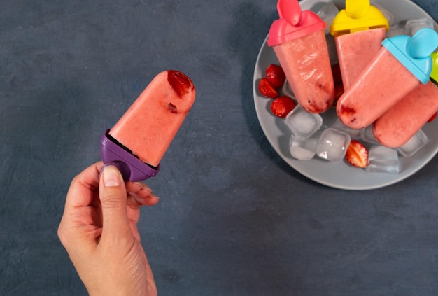 어두운 돌 배경의 냉동 과일 주스 빈티지 스타일의 꼭대기 전망에 여성의 손에 수제 딸기 아이스크림