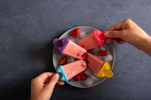 Homemade strawberry ice cream in female hands on dark stone background frozen fruit juice vintage style top view