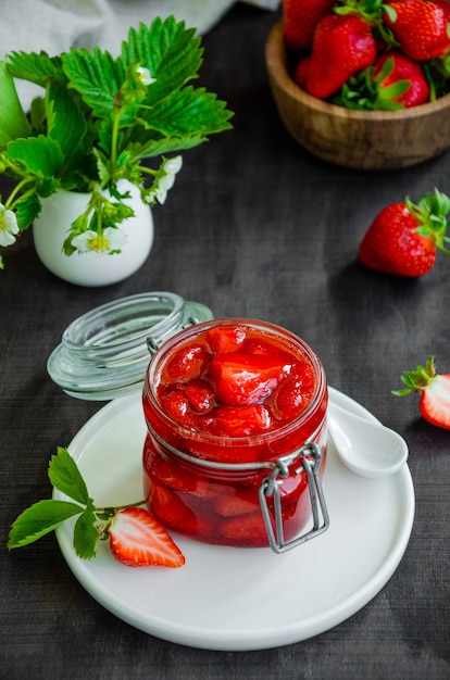 Homemade strawberry jam in a glass jar with fresh strawberries on a dark