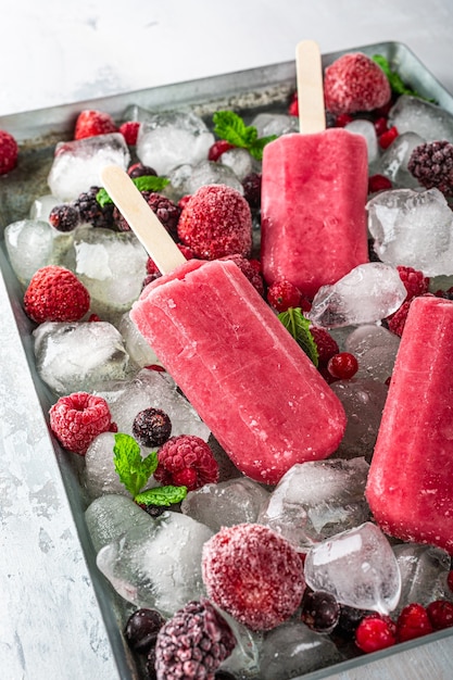 Homemade strawberry popsicles on metal plate with ice, assorted berries and mint. Healthy summer food concept with copy space