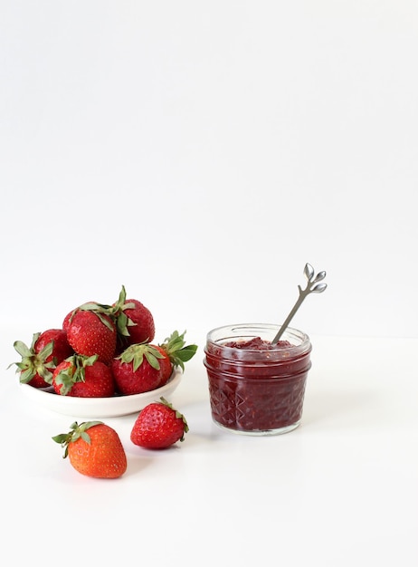 Homemade strawberry preserves or jam in a mason jar surrounded by fresh organic strawberries Selective focus with blurred foreground and background