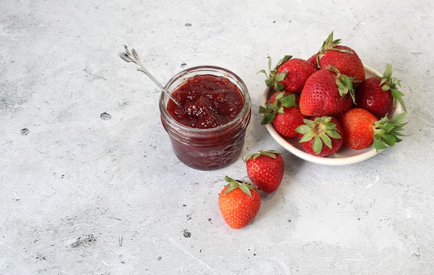 Foto conserve di fragole fatte in casa o marmellata in un barattolo di vetro circondato da fragole fresche biologiche messa a fuoco selettiva con primo piano e sfondo sfocati