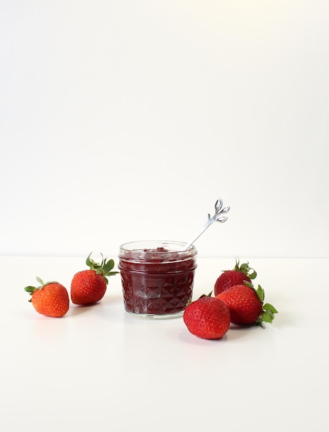 Homemade strawberry preserves or jam in a mason jar surrounded by fresh organic strawberries Selective focus with white background