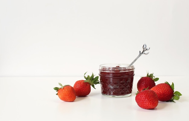 Homemade strawberry preserves or jam in a mason jar surrounded by fresh organic strawberries Selective focus with white background