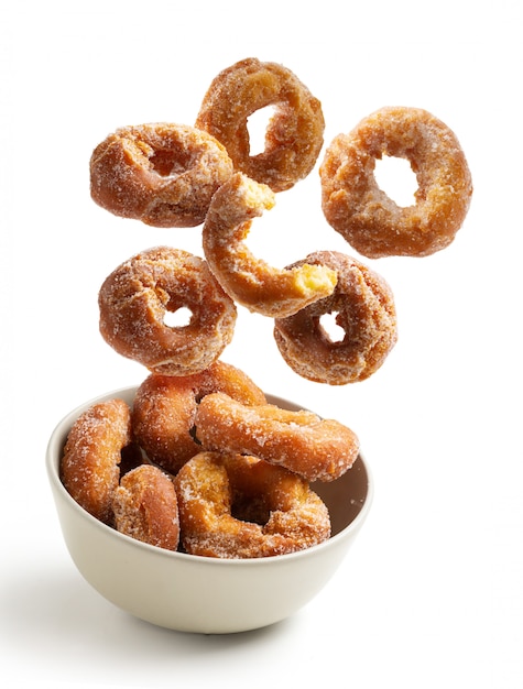 Homemade sugar doughnuts falling into a bowl