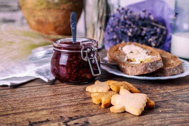 Biscotti fatti in casa miele miele, marmellata di lamponi in barattolo, pane e burro, coltello, su un fondo di legno. concetto di colazione.