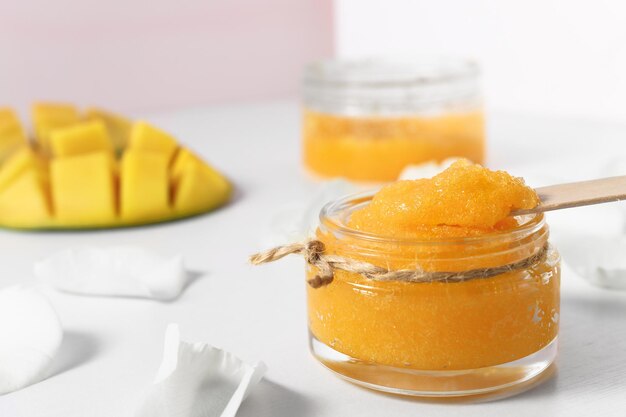 Homemade sugar scrub in a glass bowl on a white wooden table Cosmetic product of orange color